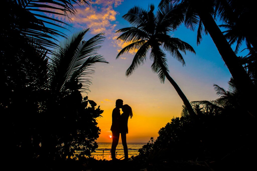 pexels-photo-1024975-1024975 Silhouette of a couple sharing a romantic moment on a tropical beach at sunset with palm trees.